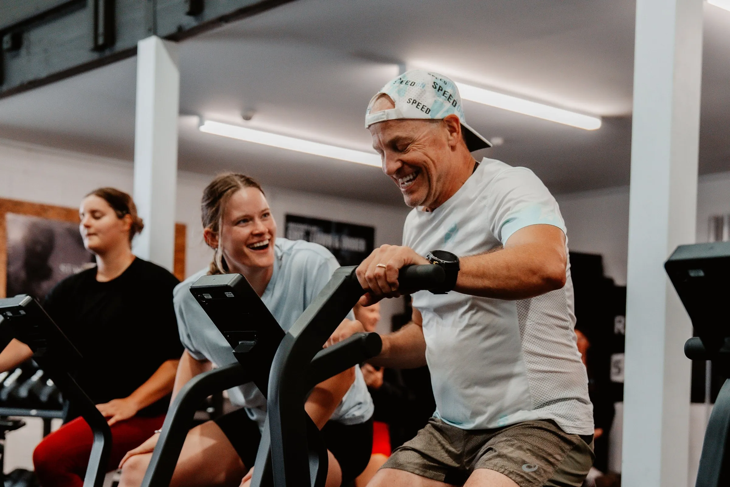 Members sharing a laugh mid-workout on the air bikes.